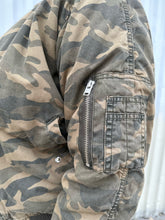 Load image into Gallery viewer, Close up view of the camo pattern of a size M (fits like 10/12) STAMPD brand camo zip-up bomber jacket on a size 14/16 model. The photo is taken outside in natural lighting.