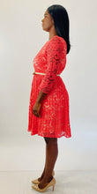 Load image into Gallery viewer, Full-body side view of a size 16 Eliza J coral lace long sleeve pleated midi dress with cream lining underneath and cream skinny belt styled with tan patent leather heels on a size 12 model.