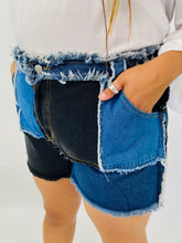 Load image into Gallery viewer, Half-side view of these size 4X SHEIN light and dark wash patchwork denim shorts with unfinished hems and distressing details on a size 18 model.