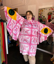 Load image into Gallery viewer, Front view showing off the length and span of the bell sleeves of a size 4XL Fashion Brand Company pink month mini dress with "Jewish Girls" cursive all-over pattern styled with black combat boots on a size 24 model. The photo is taken inside in front of a window, combining natural light and overhead lighting.