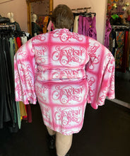 Load image into Gallery viewer, Back view of a size 4XL Fashion Brand Company pink month mini dress with "Jewish Girls" cursive all-over pattern styled with black combat boots on a size 24 model. The photo is taken inside in front of a window, combining natural light and overhead lighting.