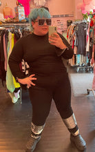 Load image into Gallery viewer, Full-body front view of a pair of size 16 Eloquii black denim straight leg jeans with silver sequin details at the ankles styled with a black turtleneck and black crocs on a size 16/18 model.