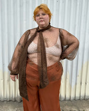 Load image into Gallery viewer, Front view of a size 22/24 Eloquii dark brown sheer puff sleeve pussybow blouse styled untucked over a pair of rust colored silky pants on a size 22/24 model. The photo is taken outside in natural lighting.
