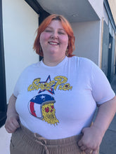 Load image into Gallery viewer, Front view of a size XL &quot;Evel Pie&quot; Evel Knievel pizza t-shirt styled tucked into brown shorts on a size 22/24 model. The photo was taken outside in natural lighting.
