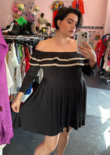Load image into Gallery viewer, Front view of a size 3X Rue 107 black and tan ruffled neckline off-the-shoulder long sleeve mini dress styled with tan heels on a size 14/16 model. The photo was taken inside under fluorescent lighting.
