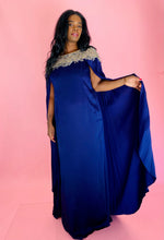 Load image into Gallery viewer, Full-body front view of a size 16 Marchesa royal purple silky caped floor-length gown with embroidered and beaded neckline and cape on a size 12 model. The photo was taken inside under photography lighting.
