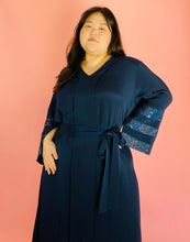 Load image into Gallery viewer, Closer front view of a size XXL Sachin &amp; Babi deep navy blue silky faux-wrap gown with long sleeves and sequin stripes on a size 14/16 model. The photo was taken indoors under studio lighting.
