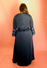 Load image into Gallery viewer, Full-body back view of a size XXL Sachin &amp; Babi deep navy blue silky faux-wrap gown with long sleeves and sequin stripes on a size 14/16 model. The photo was taken indoors under studio lighting.

