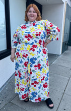 Load image into Gallery viewer, Additional full-body front view of a size 28/30W RIXO x Target collab white and rainbow floral high-necked maxi dress with a ruffled front slit on a size 22/24 model. The photo was taken outside in natural lighting.
