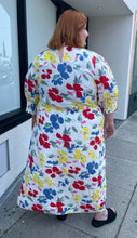 Load image into Gallery viewer, Full-body back view of a size 28/30W RIXO x Target collab white and rainbow floral high-necked maxi dress with a ruffled front slit on a size 22/24 model. The photo was taken outside in natural lighting.
