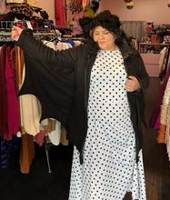 Load image into Gallery viewer, Front view showing off the connected bat wing sleeve of a size 1/2X Leg Avenue black bat costume hoodie with bat wing, connected sleeves and fuzzy ears on the hood, styled unzipped, open over a white and black polka dot dress on a size 14/16 model.
