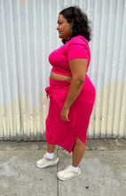 Load image into Gallery viewer, Full-body side view of a size 2 Fashion to Figure two piece hot pink cropped tee and tie-detail maxi skirt set styled with white sneakers on a size 18/20 model. The photo is taken outside in natural lighting.
