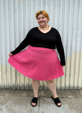 Load image into Gallery viewer, Full-body front view of a size 22/24 Eloquii bubblegum pink mini circle skirt made of sweater material styled with a long sleeve black shirt and black slides on a size 22/24 model. The photo is taken outside in natural lighting.
