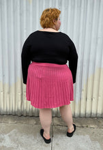 Load image into Gallery viewer, Full-body back view of a size 22/24 Eloquii bubblegum pink mini circle skirt made of sweater material styled with a long sleeve black shirt and black slides on a size 22/24 model. The photo is taken outside in natural lighting.
