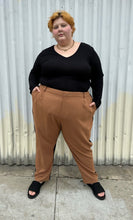 Load image into Gallery viewer, Full-body front view (where you can only see the brown side) of a pair of size 28 Eloquii half brown, half black trousers styled with a black long sleeve and black slides on a size 22/24 model. The photo is taken outside in natural lighting.

