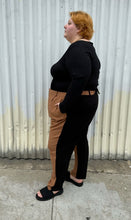 Load image into Gallery viewer, Additional full-body side view of a pair of size 28 Eloquii half brown, half black trousers styled with a black long sleeve and black slides on a size 22/24 model. The photo is taken outside in natural lighting.
