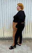 Load image into Gallery viewer, Full-body side view of a pair of size 28 Eloquii half brown, half black trousers styled with a black long sleeve and black slides on a size 22/24 model. The photo is taken outside in natural lighting.
