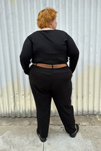 Load image into Gallery viewer, Full-body back view (where you can only see the black side) of a pair of size 28 Eloquii half brown, half black trousers styled with a black long sleeve and black slides on a size 22/24 model. The photo is taken outside in natural lighting.
