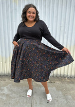 Load image into Gallery viewer, Full-body front view of a size 4X (fits like 2X) Banned Retro black maxi skirt with orange, purple, and white mixed Halloween pattern featuring cats with witch hats styled with a black long sleeve and white mules on a size 18/20 model. The photo was taken outside in natural lighitng.
