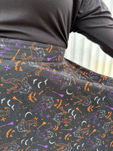 Load image into Gallery viewer, Close up on the mixed Halloween print of a size 4X (fits like 2X) Banned Retro black maxi skirt with orange, purple, and white mixed Halloween pattern featuring cats with witch hats on a size 18/20 model. The photo was taken outside in natural lighting.
