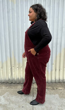 Load image into Gallery viewer, Full-body side view of a pair of size 26 (fits like 18/20) Ulla Popken maroon corduroy overalls styled over a black long sleeve and boots on a size 18/20 model. The photo is taken outside in natural lighting.
