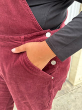 Load image into Gallery viewer, Close view of the corduroy texture and front pockets of a pair of size 26 (fits like 18/20) Ulla Popken maroon corduroy overalls on a size 18/20 model. The photo is taken outside in natural lighting.
