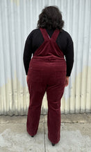 Load image into Gallery viewer, Full-body back view of a pair of size 26 (fits like 18/20) Ulla Popken maroon corduroy overalls styled over a black long sleeve and boots on a size 18/20 model. The photo is taken outside in natural lighting.
