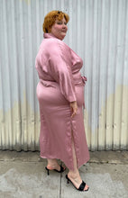 Load image into Gallery viewer, Full-body side view of a size 22/24 Eloquii blush pink silky faux wrap maxi dress with a belt styled with black kitten heels on a size 22/24 model. The photo was taken outside in natural lighting.
