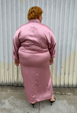 Load image into Gallery viewer, Full-body back view of a size 22/24 Eloquii blush pink silky faux wrap maxi dress with a belt styled with black kitten heels on a size 22/24 model. The photo was taken outside in natural lighting.
