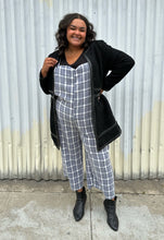 Load image into Gallery viewer, Full-body front view of a size 18 City Chic black collarless longline zip-up jacket with pleather accents styled open over a blue &amp; white plaid jumpsuit and black boots on a size 18/20 model. The photo was taken outside in natural lighting.

