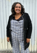 Load image into Gallery viewer, Front view of a size 18 City Chic black collarless longline zip-up jacket with pleather accents styled open over a blue &amp; white plaid jumpsuit on a size 18/20 model. The photo was taken outside in natural lighting.
