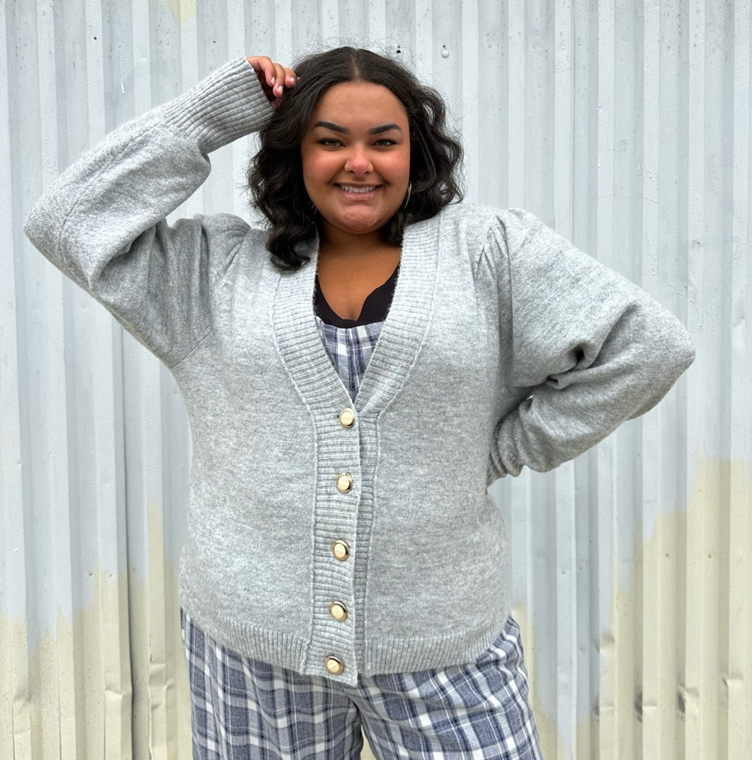 Front view of a size 22/24 Eloquii light gray cardigan with pearl & gold buttons styled over a blue & white plaid jumpsuit on a size 18/20 model. The photo was taken outside in natural lighting.