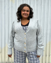 Load image into Gallery viewer, Additional front view of a size 22/24 Eloquii light gray cardigan with pearl &amp; gold buttons styled over a blue &amp; white plaid jumpsuit on a size 18/20 model. The photo was taken outside in natural lighting.
