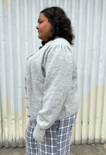 Load image into Gallery viewer, Side view of a size 22/24 Eloquii light gray cardigan with pearl &amp; gold buttons styled over a blue &amp; white plaid jumpsuit on a size 18/20 model. The photo was taken outside in natural lighting.
