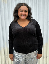 Load image into Gallery viewer, Additional front view of a size 18/20 Eloquii black velvet long sleeve v-neck top with silver metallic threading throughout styled over silver sequin trousers on a size 18/20 model. The photo was taken outside in natural lighting.
