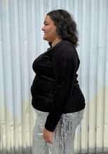 Load image into Gallery viewer, Side view of a size 18/20 Eloquii black velvet long sleeve v-neck top with silver metallic threading throughout styled over silver sequin trousers on a size 18/20 model. The photo was taken outside in natural lighting.
