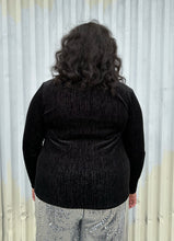 Load image into Gallery viewer, Back view of a size 18/20 Eloquii black velvet long sleeve v-neck top with silver metallic threading throughout styled over silver sequin trousers on a size 18/20 model. The photo was taken outside in natural lighting.
