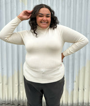 Load image into Gallery viewer, Front view of a size 2 Fashion to Figure cream turtleneck sweater styled with black trousers on a size 18/20 model. The photo was taken outside in natural lighting.
