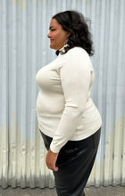 Load image into Gallery viewer, Side view of a size 2 Fashion to Figure cream turtleneck sweater styled with black trousers on a size 18/20 model. The photo was taken outside in natural lighting.
