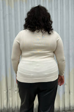 Load image into Gallery viewer, Back view of a size 2 Fashion to Figure cream turtleneck sweater styled with black trousers on a size 18/20 model. The photo was taken outside in natural lighting.
