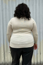 Load image into Gallery viewer, Back view of a size 2 Fashion to Figure cream turtleneck sweater styled with black trousers on a size 18/20 model. The photo was taken outside in natural lighting.
