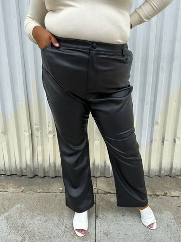 Front view of a size 24 (fits like 20/22) Eloquii black pleather straight leg pants styled with a cream turtleneck and white mules on a size 18/20 model. The photo was taken outside in natural lighting.