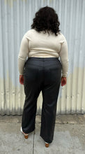 Load image into Gallery viewer, Full-body back view of a size 24 (fits like 20/22) Eloquii black pleather straight leg pants styled with a cream turtleneck and white mules on a size 18/20 model. The photo was taken outside in natural lighting.
