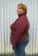 Load image into Gallery viewer, Side view of a size 4 Fashion to Figure x Gabi Fresh maroon &amp; off-white 70s floral turtleneck top styled over medium wash denim on a size 22/24 model. The photo is taken outside in natural lighting.
