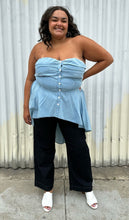 Load image into Gallery viewer, Full-body front view of a size 2 Fashion to Figure chambray strapless button-up high-low blouse styled over dark wash denim and white mules on a size 18/20 model. The photo was taken outside in natural lighting.
