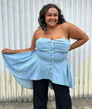 Load image into Gallery viewer, Front view of a size 2 Fashion to Figure chambray strapless button-up high-low blouse styled over dark wash denim on a size 18/20 model. The photo was taken outside in natural lighting.

