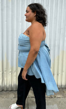 Load image into Gallery viewer, Side view of a size 2 Fashion to Figure chambray strapless button-up high-low blouse styled over dark wash denim on a size 18/20 model. The photo was taken outside in natural lighting.
