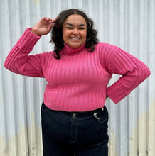 Load image into Gallery viewer, Front view of a size 18/20 Eloquii bubblegum pink ribbed turtleneck cropped sweater styled over a dark wash denim trouser on a size 18/20 model The photo was taken outside in natural lighting.

