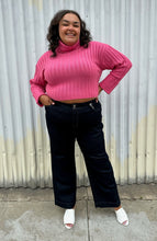 Load image into Gallery viewer, Full-body front view of a size 18/20 Eloquii bubblegum pink ribbed turtleneck cropped sweater styled over a dark wash denim trouser and white mules on a size 18/20 model The photo was taken outside in natural lighting.

