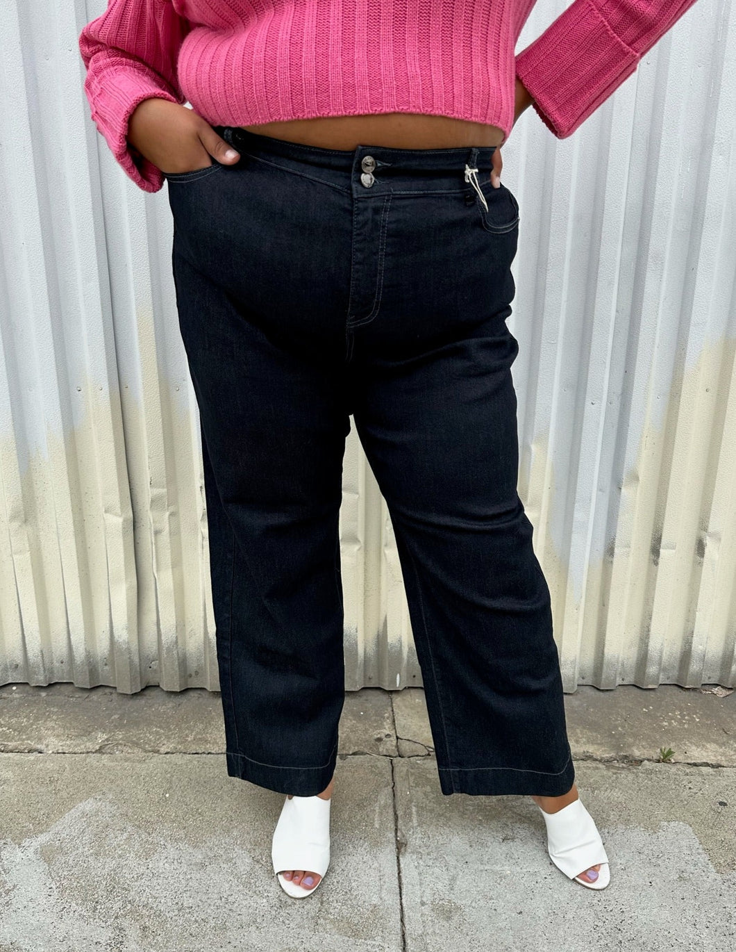 Front view of a pair of size 20 DC Jeans dark wash wide leg denim styled with a bubblegum pink cropped sweater and white mules on a size 18/20 model. The photo was taken outside in natural lighting.